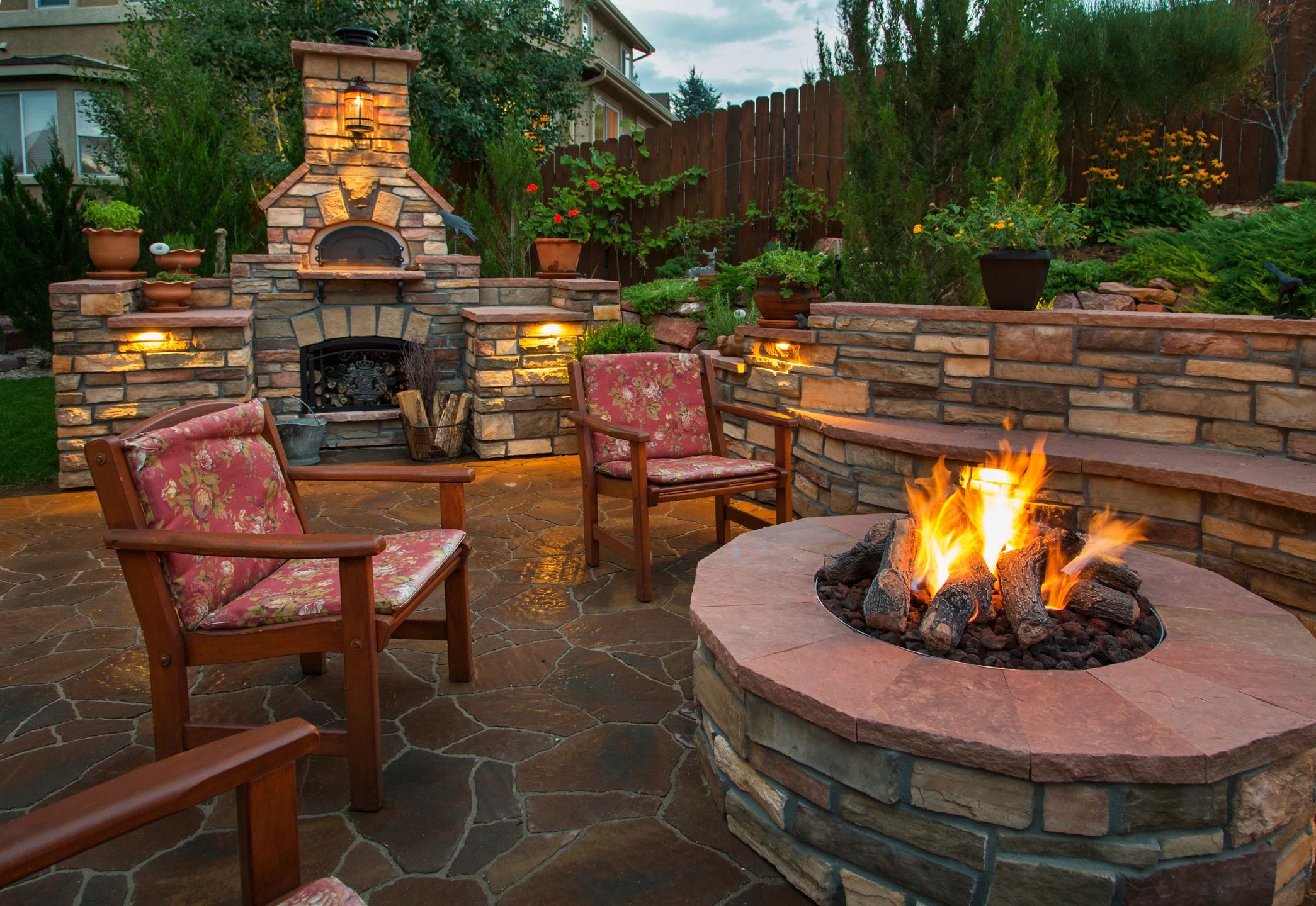 Stone fireplace and firepit surrounded by bushes and flowers in outdoor area